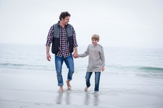 Father and son walking in shallow water at sea shore