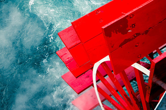 Steam ship on a cruise. Bright red wooden paddle wheels splash into the vivid blue clear waters. Motion blur. High contrast. Travel, abstract, nautical, coastal, fashion, 