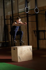 Man doing crossfit exercise. He jumping on wooden box.