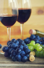 Two glasses with red wine, bottle of wine, grapes and wine traffic jams on a wooden surface