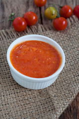 Homemade tomato sauce in white bowl on hemp sack with raw tomatoes