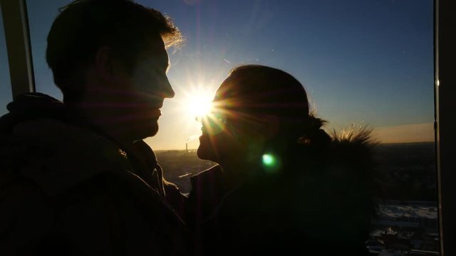 Romantic young couple silhouette is kissing on a sunset with sun shining bright behind them on a horizon, city background