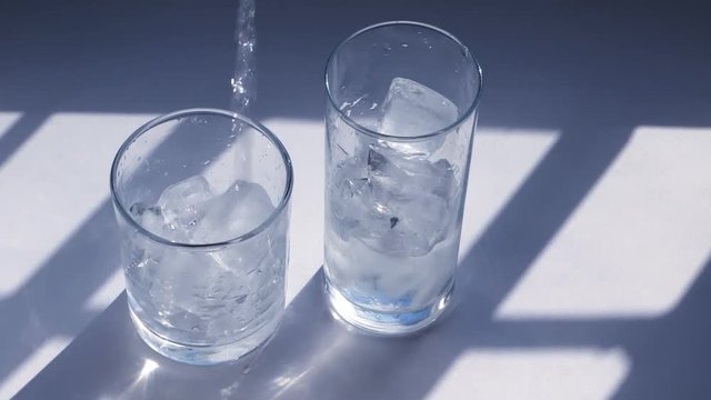 Cold blue water being poured in glasses with ice. Sunlight, highlights, shades,