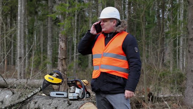 Lumberjack talking on cell phone near chainsaw in forest