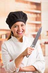 Woman chef wearing cooking outfit posing happily holding large metal kitchen knife