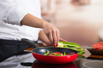 Closeup chef hand adding salt to vegetables frying inside red skillet