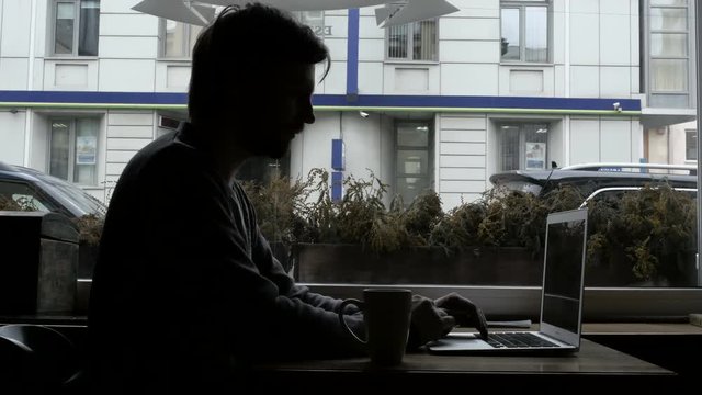 Silhouette of Happy Young Man Freelancer with Modern Laptop in Cafe taking Cup of Coffee
