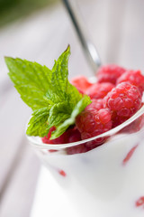 Yogurt topped with fresh raspberries and mint leaves in a glass