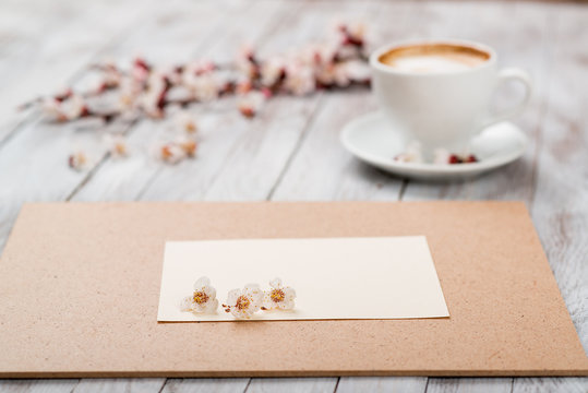 A cup of coffee next to the spring white flowers on wooden texture. Space for text.
