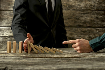 Businessman pointing to falling dominos and his partner stopping