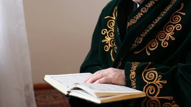 An old mullah in national dress reading the Koran. Slow motion