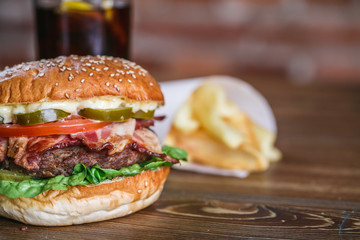 Close up on fresh burger in bun with sesame with lettuce, tomato, beef and bacon.