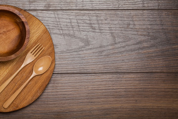 Empty wooden bowl, fork, spoon, cutting board on nature wooden table, top view, background, template, food display montage, free space for text