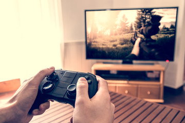 Playing game on console - hands holding game pad and playing shooter game on tv screen.