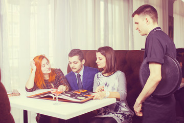 Waiter explaining the menu to a couple at the restaurant.