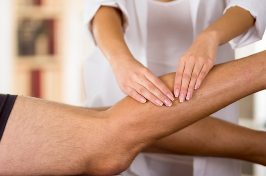 Closeup Female Physio Therapist Hands Working On Male Patients Legs, Blurry Clinic Background