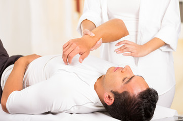 Male patient lying down with female physio therapist hands performing some stretch excercises on mans arm