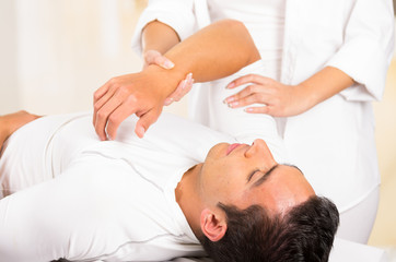 Male patient lying down with female physio therapist hands performing some stretch excercises on mans arm
