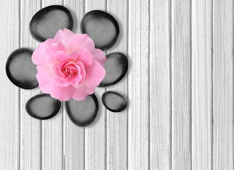 Obraz na płótnie Canvas Black spa stones and pink rose on white wooden background