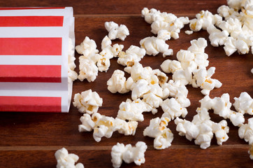 Red white striped container box lying tipped over on wooden surface with popcorn spread out