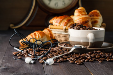 Having coffee and croissants with smartphone and headphones