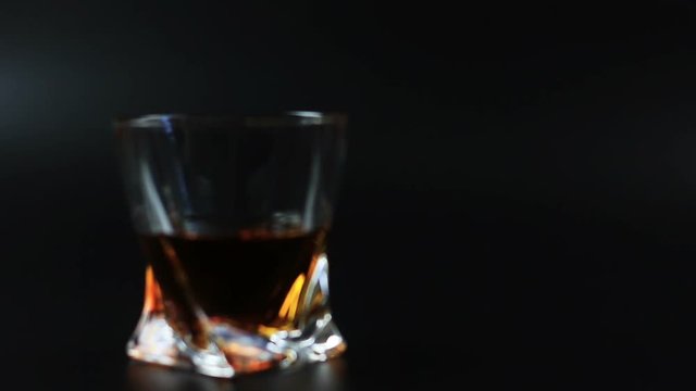 Whiskey being poured into a glass against black background. Long shot. 