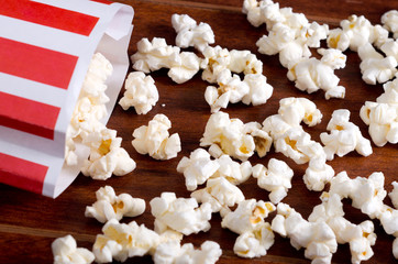 Red white striped container box lying tipped over on wooden surface with popcorn spread out