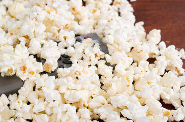 Closeup pile of white fluffy popcorn with tv remote control in the middle
