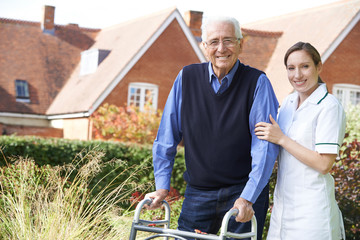 Carer Helping Senior Man To Walk In Garden Using Walking Frame