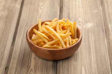 French fries in a wooden bowl, on a wooden background.