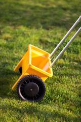 Rasen Gras d&uuml;ngen mit gelbem Streuwagen