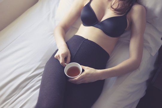 Young woman in underwear drinking tea on bed