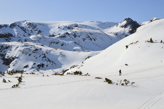 Winter in Rila Mountain, Bulgaria. Hiker walking in the snow. The Hut “Seven Rila Lakes” seen on a distant hill.
