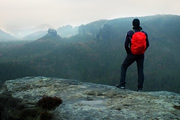 Hiker with red backpack on sharp sandstone rock in rock empires park and watching over the misty and foggy spring valley