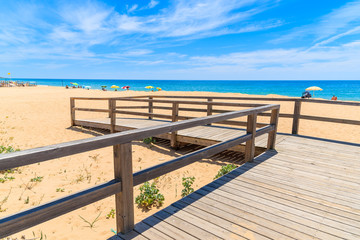 Fototapeta na wymiar Wooden footbridge to sandy beach in Armacao de Pera coastal town, Algarve region, Portugal