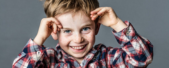 portrait of a cheeky young male preschooler with freckles and blue eyes playing with his hands for...
