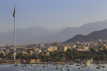 Elevated view of Aqaba seafront with huge Jordanian flag, boats and hazy mountains in distance, Aqaba, Jordan