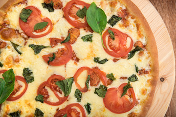 Pizza Margherita with tomatoes, mozzarella and basil on a wooden board, top view, close-up