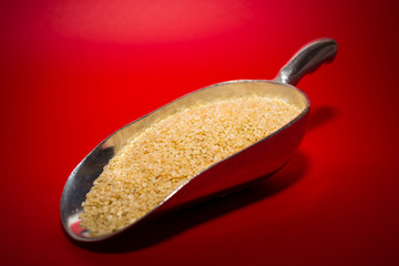 Dry and white sesame seeds in a big metal spoon on the red background