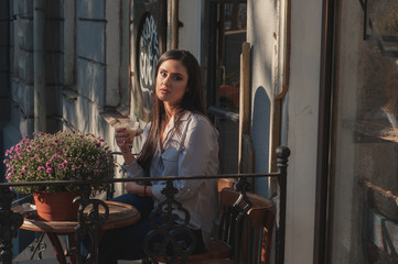 Portrait of beautiful sexy happy brunette model girl sitting in the cafe coffee shop with cup of cappuccino alone during sunny warm day 