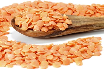 Löffel aus Olivenholz mit ungekochten roten Linsen auf weißem Hintergrund