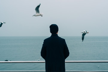 cool trendy stylish sexy handsome hipster lonely guy looking at the calm sea with seagulls back...