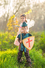 Cute little children dressed up as a knight and a fairy playing in the woods