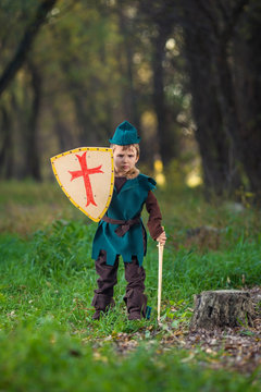 Cute little boy dressed as a knight playing with a sword and a shield in the forest