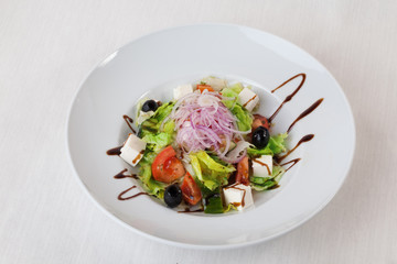 Greek salad with olives tomato cucumber lettuce balsamic sauce on top isolated white background