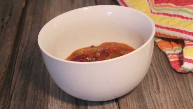 pouring chili con carne in a bowl closeup video on a wooden material background table