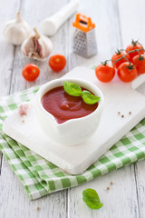 Fresh homemade tomato sauce in a white bowl on a white board, closeup, selective focus.