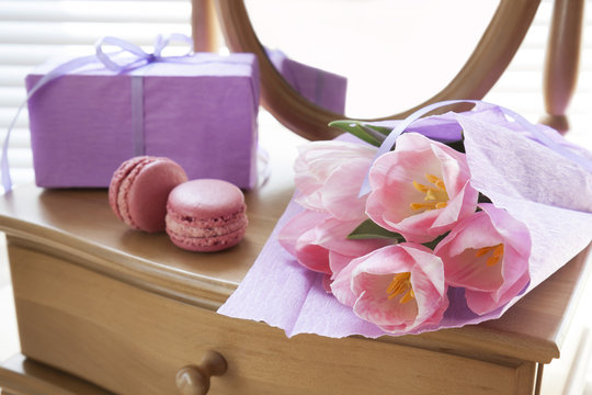 Pink tulips in violet paper, two pink macaroons, gift and mirror, backlight background