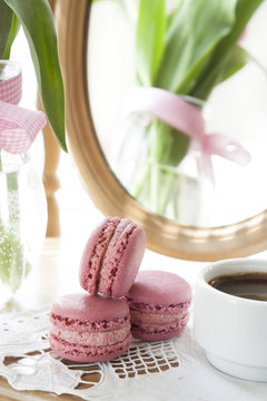 Three pink macaroons and cup of coffee, pink tulips and mirror, backlight background