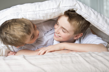 boy hiding in bed under a white blanket or coverlet.